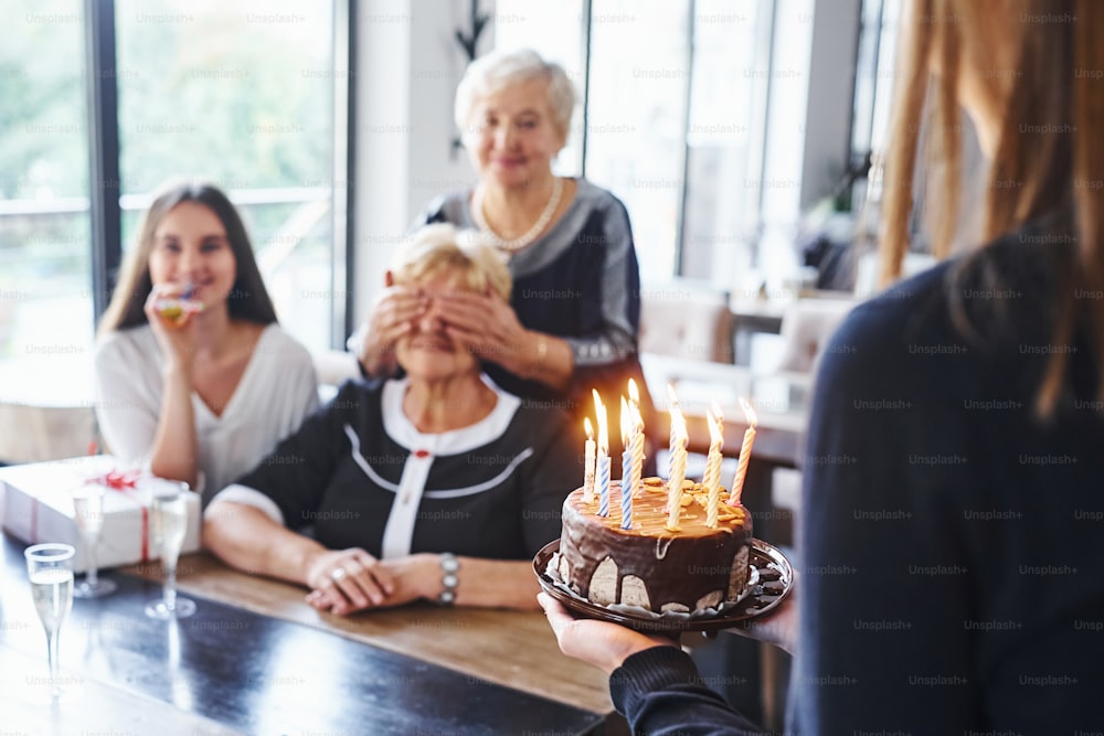 Ältere Frau mit Familie und Freunden, die drinnen Geburtstag feiern.