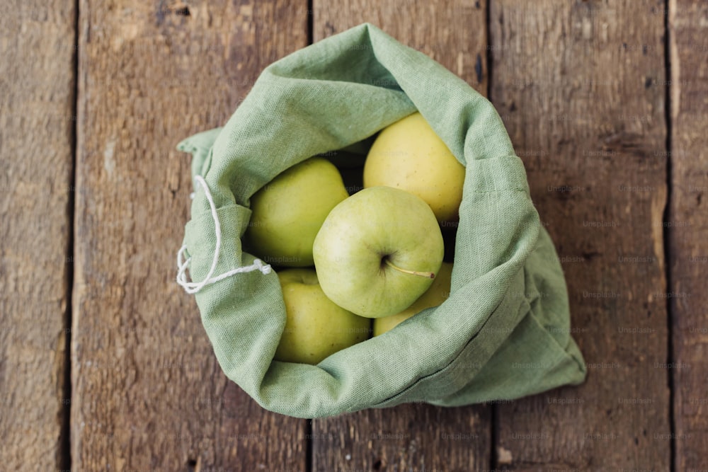 Fresh apples in eco cotton bag on rustic wooden table. Zero waste shopping concept. Ban plastic. Organic apples in green reusable bag, top view. Eco sustainable lifestyle