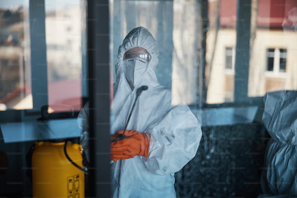 Front view of a cleaner in a hazmat suit and rubber gloves holding a manual pressure sprayer