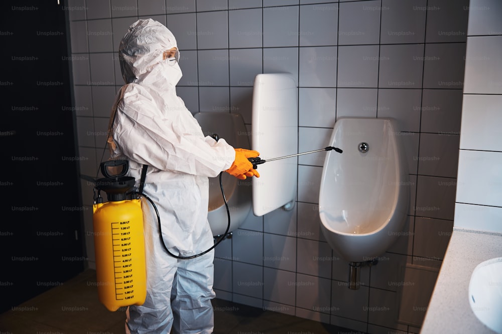 Side view of a female worker in a hazmat suit and safety goggles doing the disinfection cleaning