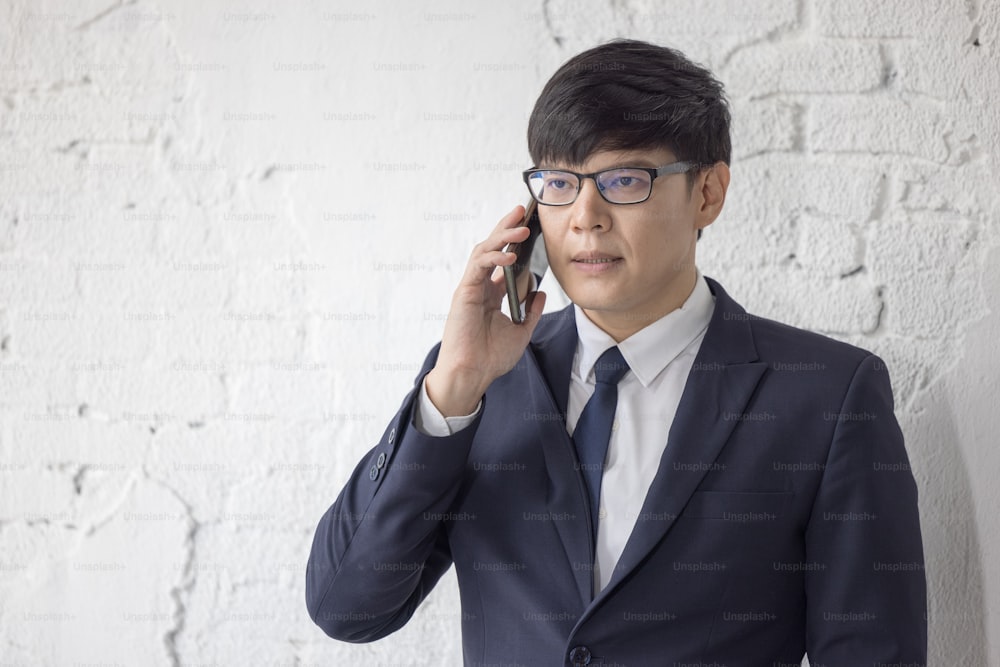 Business man talk to cellphone at office and white brick wall background."n