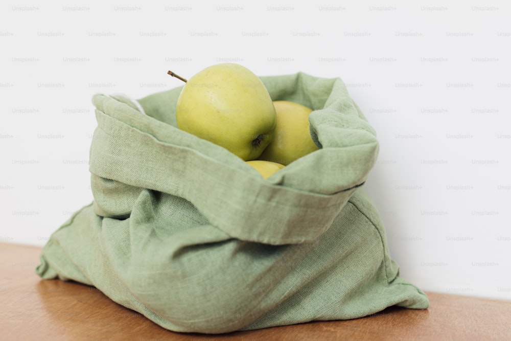 Fresh apples in cotton bag on wooden table. Zero waste shopping. Organic fruits in reusable green bag. Eco friendly plastic free grocery.  Sustainable lifestyle
