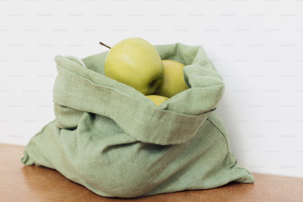 Frische Äpfel im Baumwollbeutel auf Holztisch. Zero Waste Shopping. Bio-Früchte in wiederverwendbarem grünen Beutel. Umweltfreundliches plastikfreies Lebensmittelgeschäft.  Nachhaltiger Lebensstil
