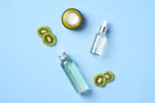 Cosmetics lotions, jar of moisturizer cream and sliced kiwi fruit on blue background. Natural organic beauty products set. Flat lay, top view.