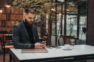 Joven y guapo hombre de negocios usando un teléfono inteligente mientras trabaja en un café