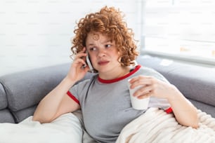 Young woman getting bad news by phone. unhappy woman talking on mobile phone looking down. Crying depressed girl holds phone sitting on sofa hopeless , breaking up, scared of threatening, mobile abuse