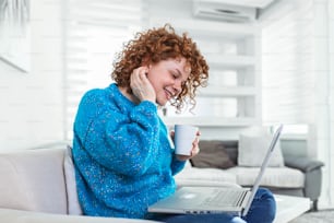 Positive young woman freelancer watching video in blog on netbook and having a coffee at comfortable home. Beautiful young business woman working on laptop.Freelancer connecting to internet