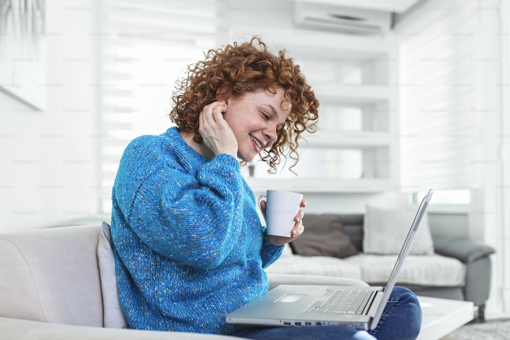 Positive young woman freelancer watching video in blog on netbook and having a coffee at comfortable home. Beautiful young business woman working on laptop.Freelancer connecting to internet