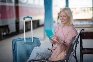 Smiling blond woman  on train station using digital tablet.