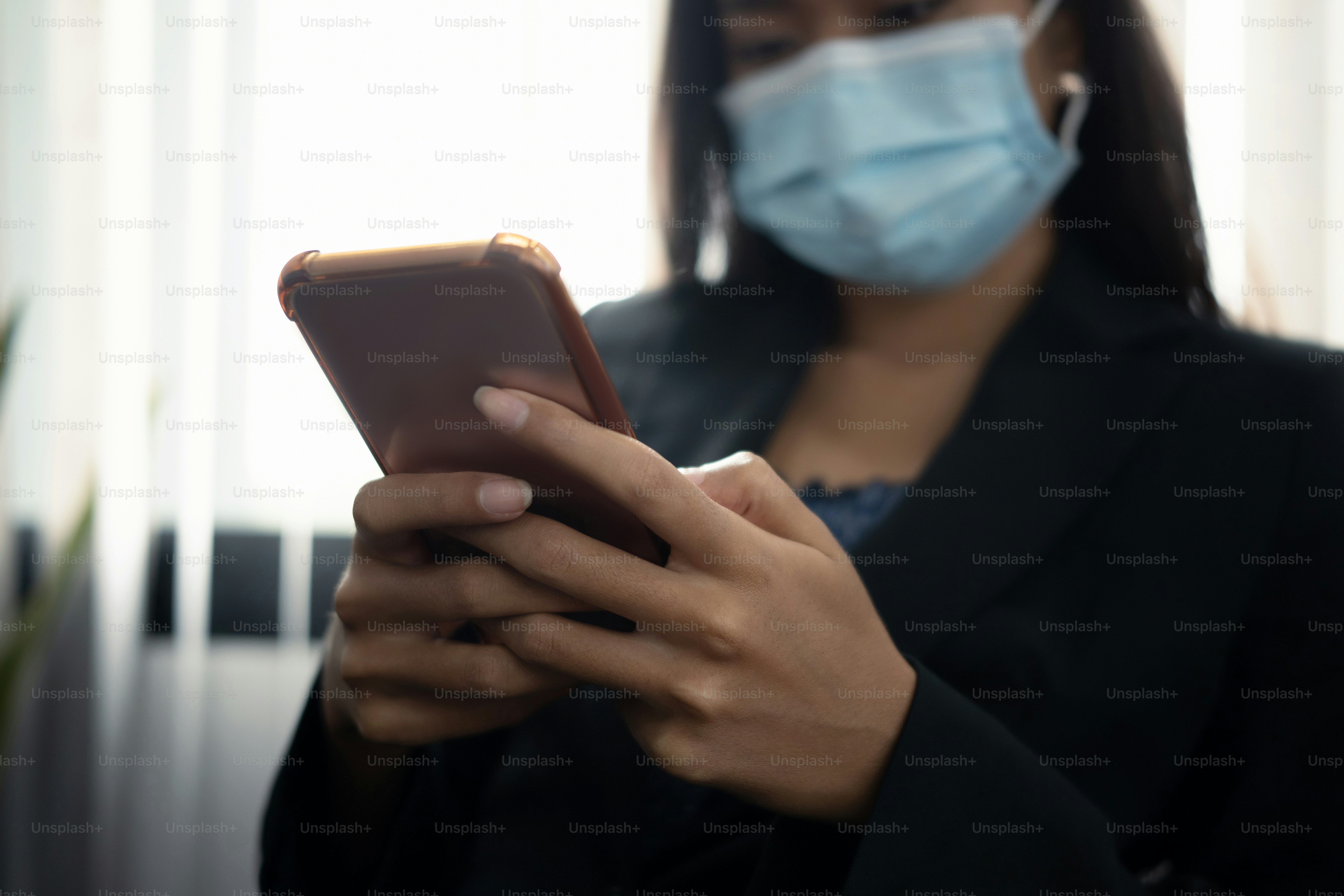 Cropped shot of businesswoman in protective mask using mobile phone in office