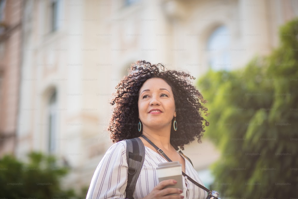 Woman with camera standing on street and drinking coffee.