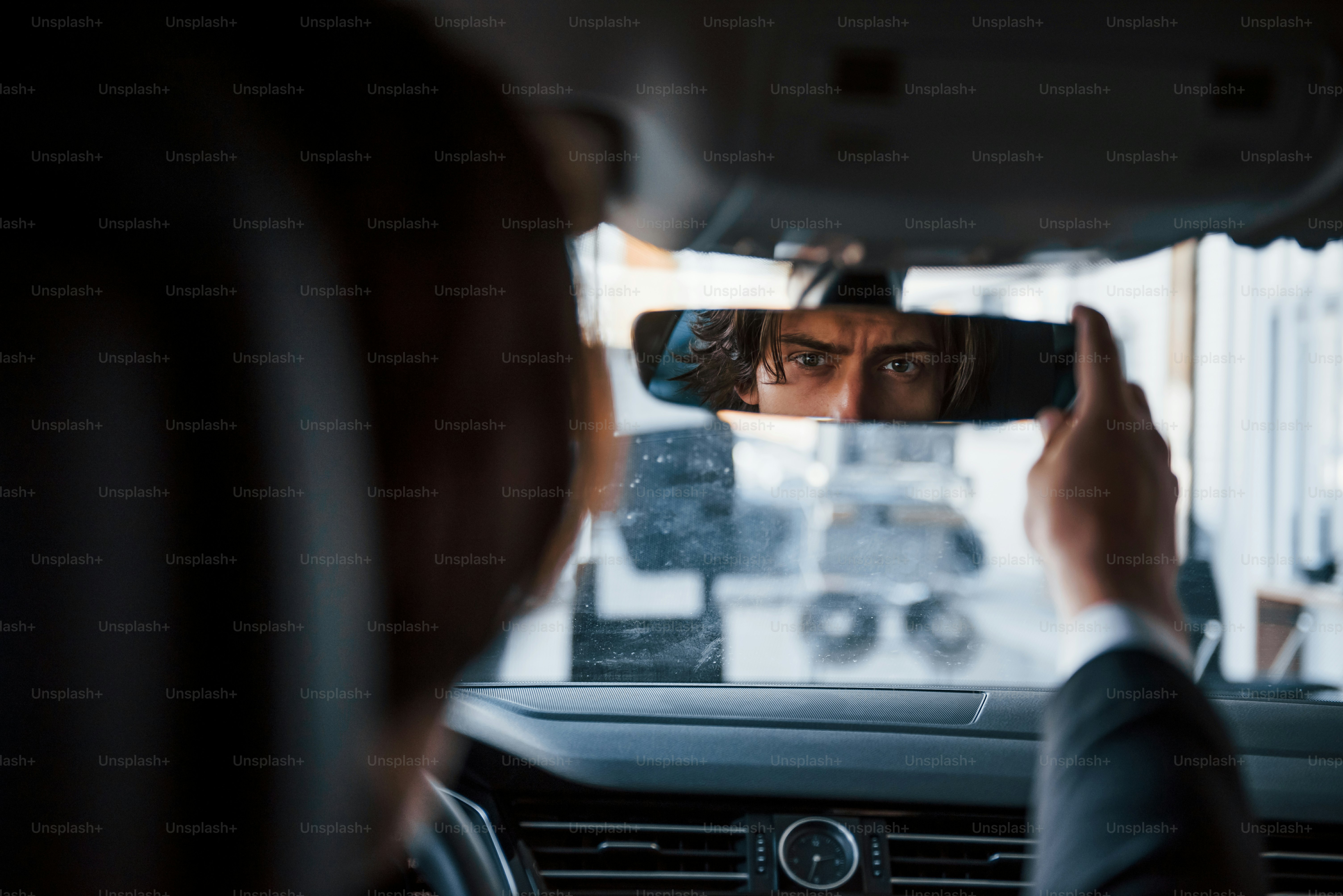 Joven hombre de negocios con traje negro y corbata conduciendo un automóvil moderno.
