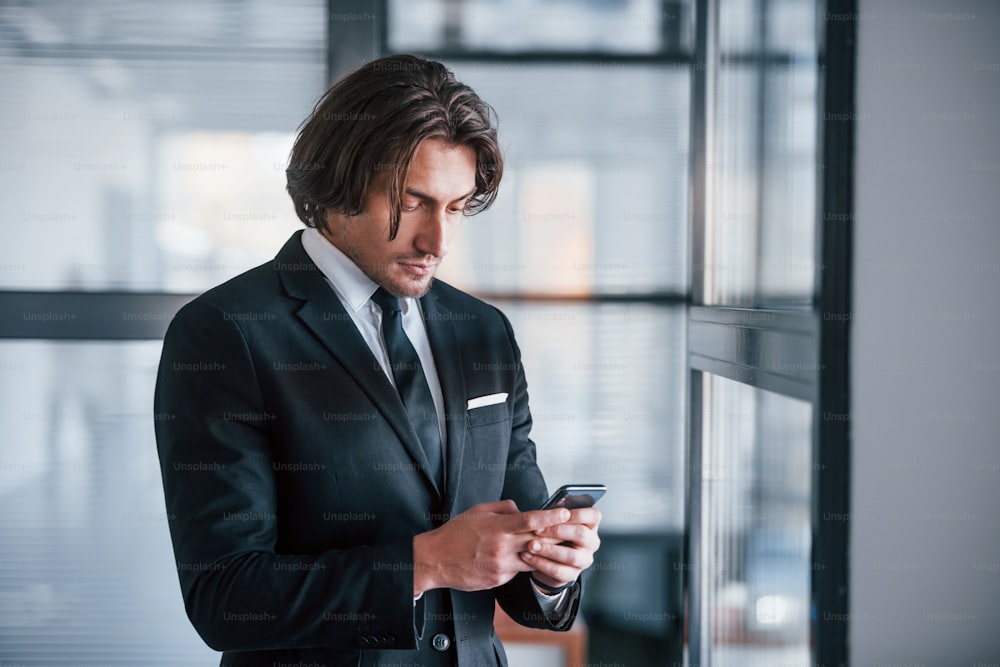 Mit dem Telefon. Porträt eines gutaussehenden jungen Geschäftsmannes in schwarzem Anzug und Krawatte.