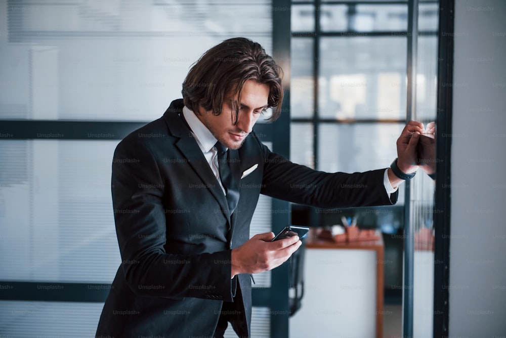 Usando el teléfono. Retrato de un joven hombre de negocios guapo con traje negro y corbata.