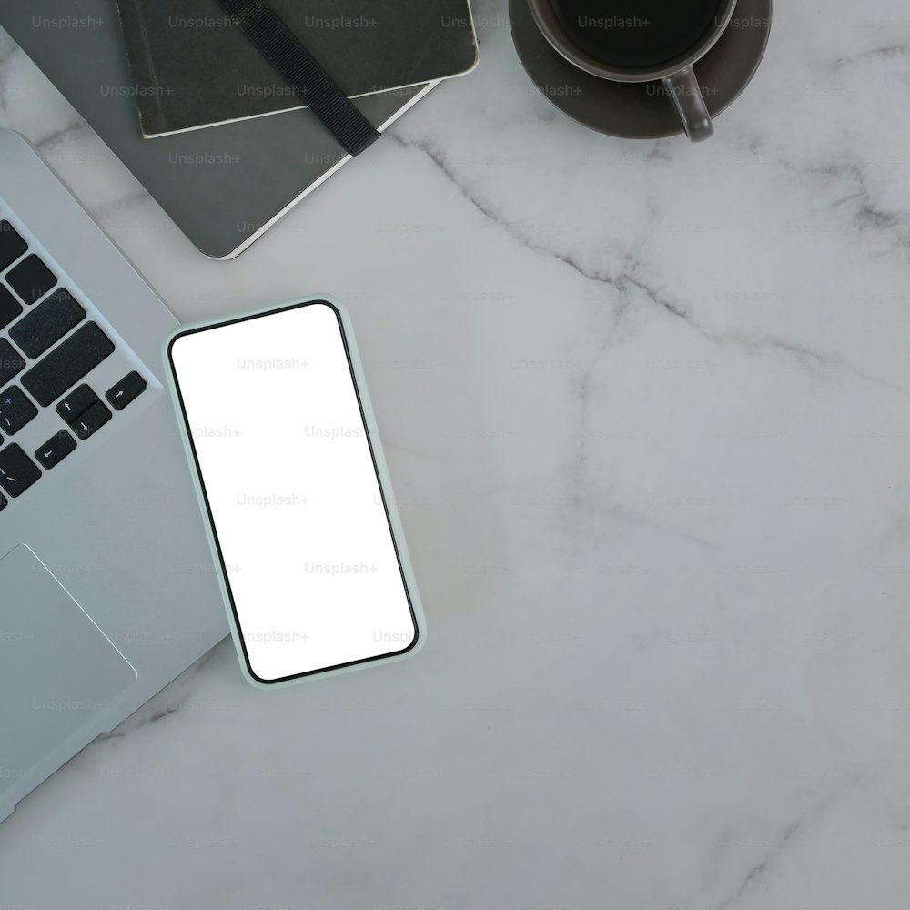 Photo carrée d’un téléphone intelligent avec écran vide, d’un ordinateur portable, d’une tasse à café et d’un ordinateur portable sur une table en marbre.