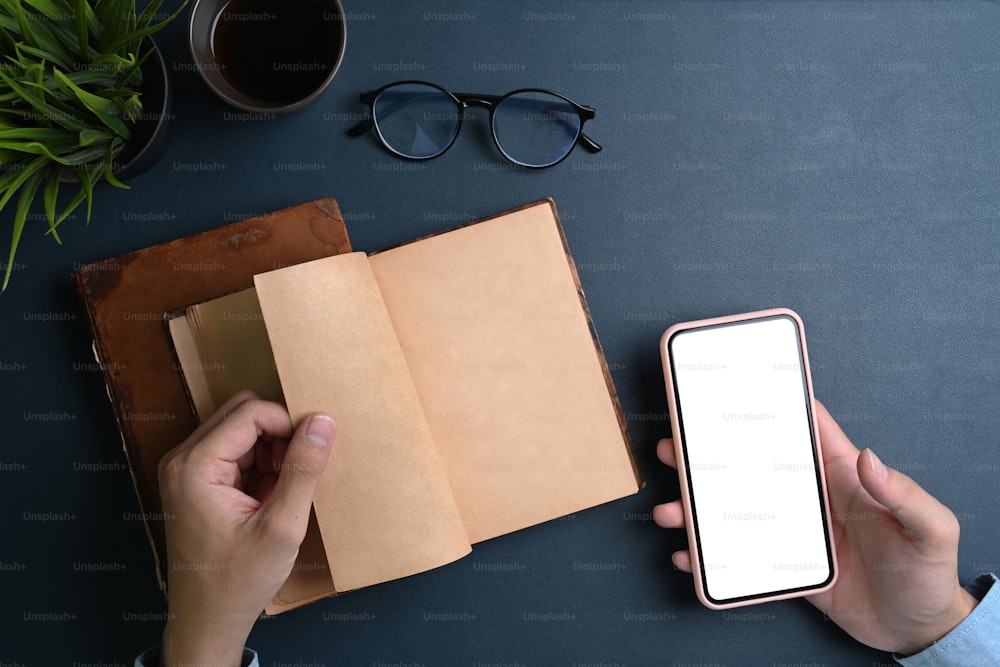 Manos de mujer sosteniendo un teléfono inteligente simulado y abriendo un cuaderno en cuero negro.