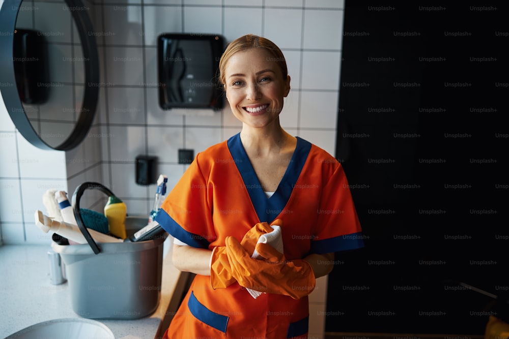 Front view of a cheerful female worker with a microfiber cloth in her hands looking ahead