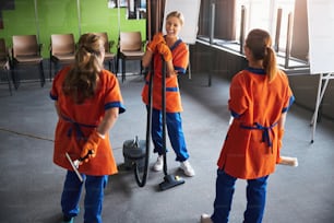 Laughing attractive female cleaner and her colleagues standing with cleaning tools in the conference room