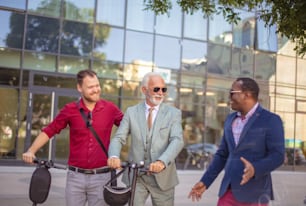 Conversa alegre.  Três homens de negócios na rua. Dois homens com scooter elétrico.