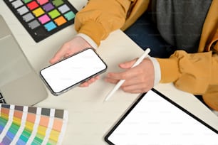 Cropped shot of female designer hands working with smartphone on office desk with tablet and designer supplies, clipping path