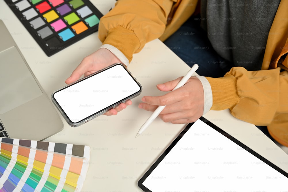 Cropped shot of female designer hands working with smartphone on office desk with tablet and designer supplies, clipping path