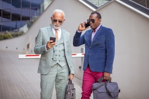 Men using mobile on street.  Two business men outdoors.