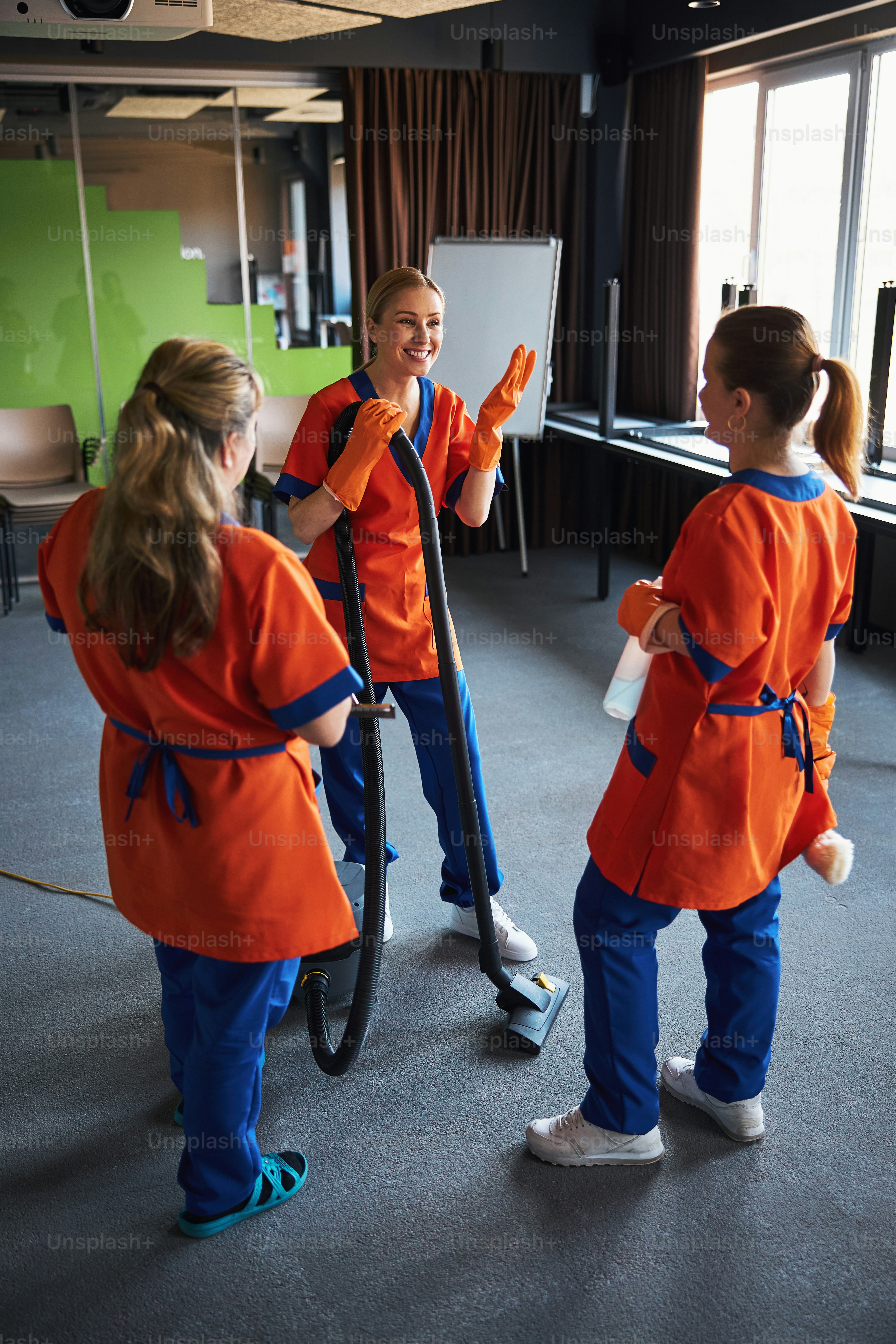 Merry cute female cleaner in the rubber gloves gesticulating during the conversation with her colleagues
