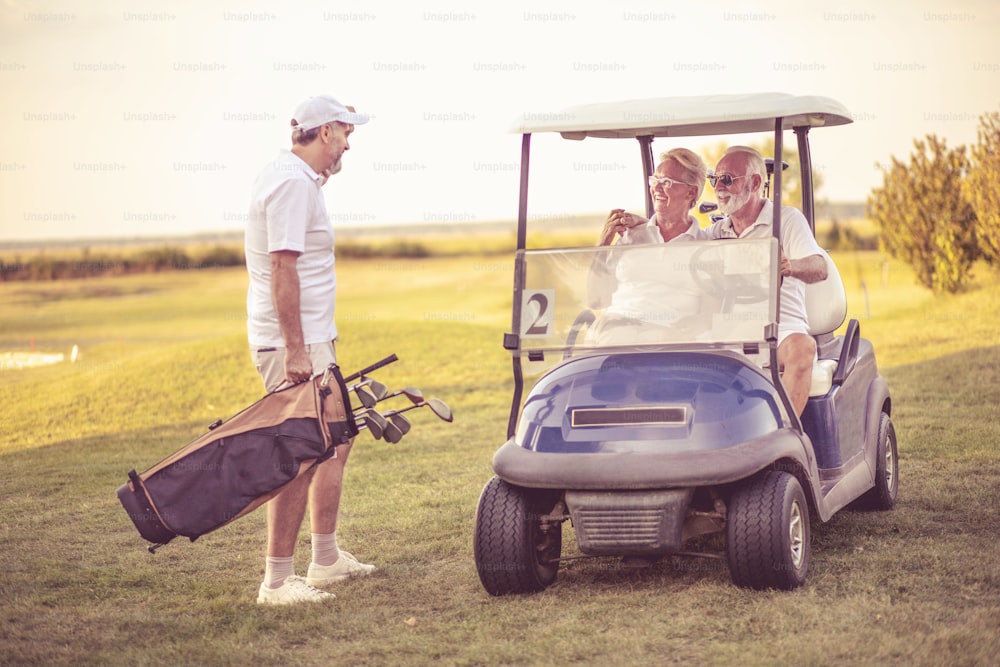 Trois golfeurs seniors. Homme et femme dans une voiture de golf.