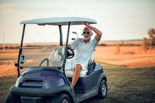Senior man driving golf car.
