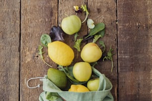 Eco friendly zero waste shopping concept. Fresh apples, lemon, avocado, salad leaves scattered from eco cotton bag on rustic wood. Salad ingredients. Organic fruits, vegetables and greenery