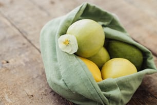 Zero waste shopping concept. Fresh apples, avocado, lemons in eco cotton bag with flower on rustic wooden table. Organic fruits and vegetables in green reusable bag. Eco friendly plastic free