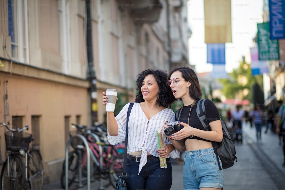 Smiling women standing on the street with cup of coffee and camera in hands.