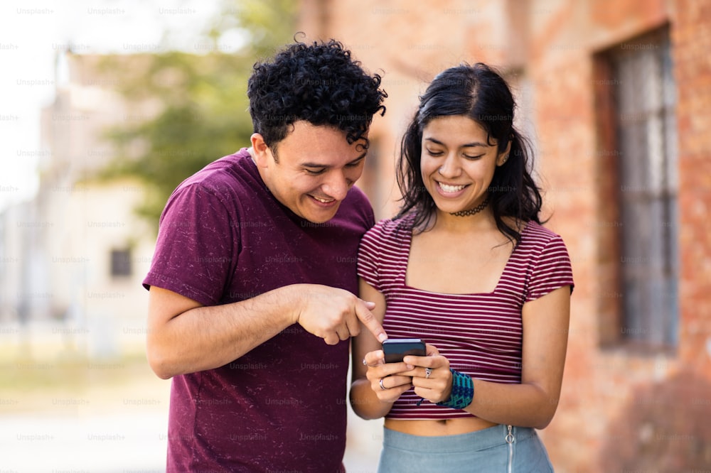 Giovane coppia sorridente sulla strada usando il cellulare.