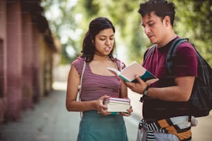 Two young students standing on street with books and talking.
