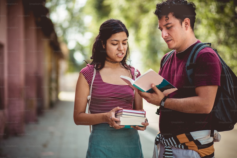 Two young students standing on street with books and talking.