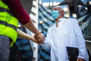 Engineer, and doctor on street handshaking. Wearing protective mask. Focus background.