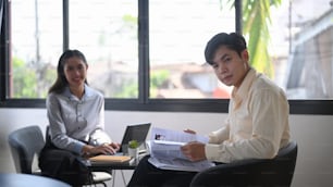 Two business people sitting together in office and looking at camera.