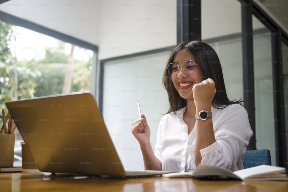 Happy successful businesswoman raising arms for celebrating startup success and looking at laptop computer.