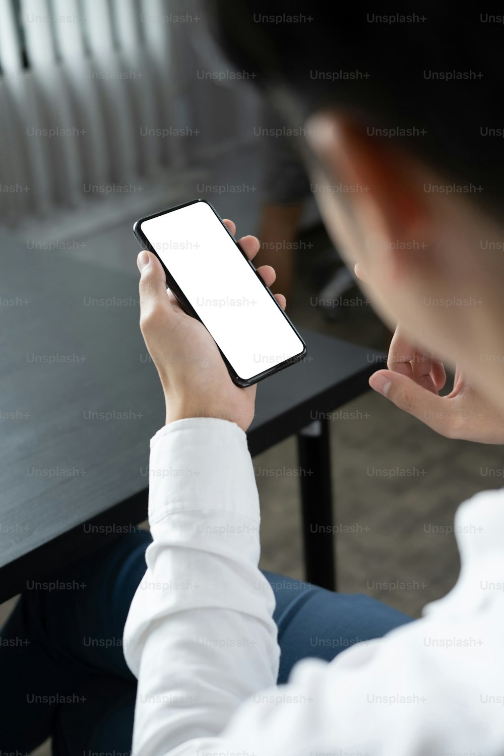 Vista de cerca sobre el hombro de un hombre de negocios sosteniendo un teléfono móvil simulado con la pantalla vacía.