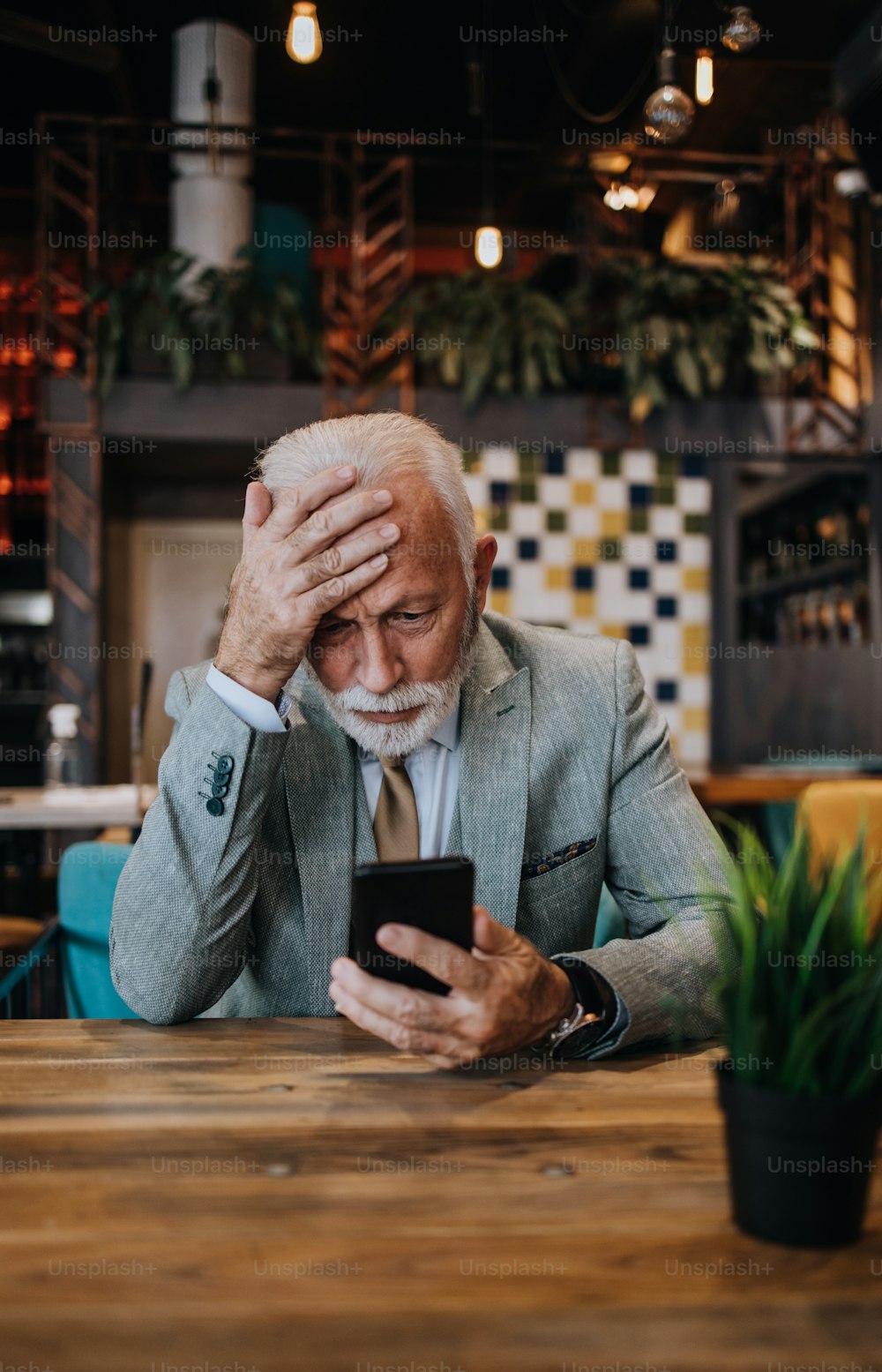 Happy and handsome senior businessman sitting in restaurant and waiting for lunch. He is using smart phone and talking with someone. Business seniors lifestyle concept.