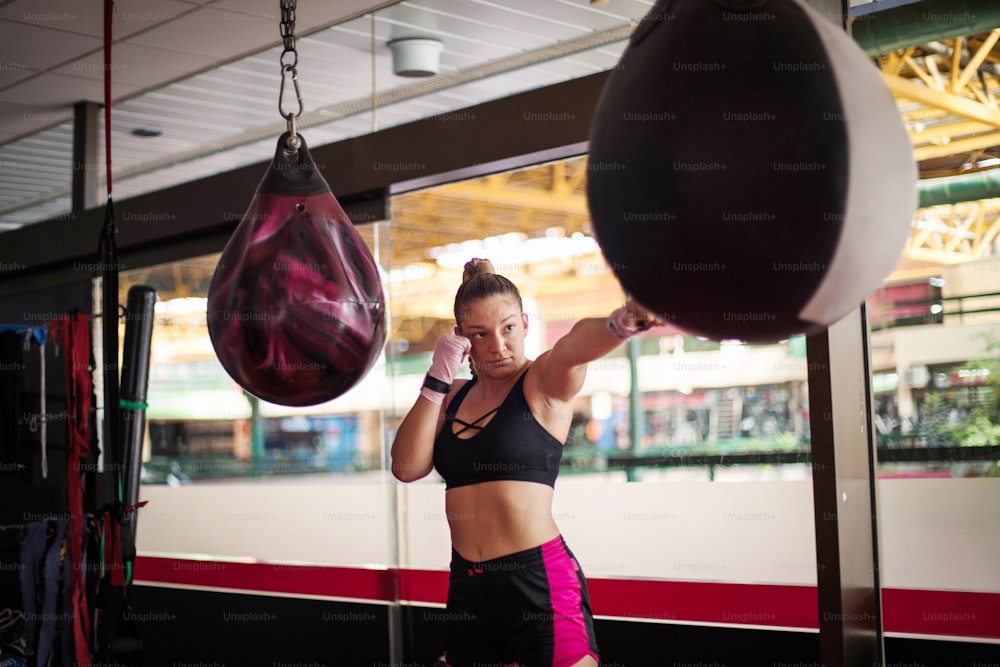 Strong young lady with boxing gloves, punching bag in gym alone.