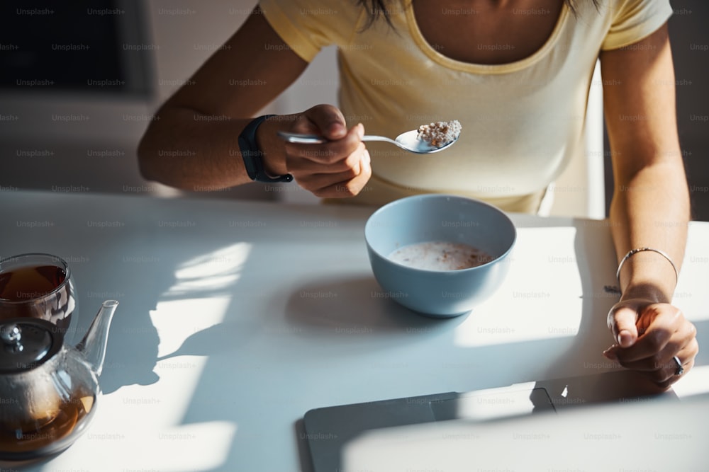 Close up of female person with spoon in her hand sitting at the table and having breakfast