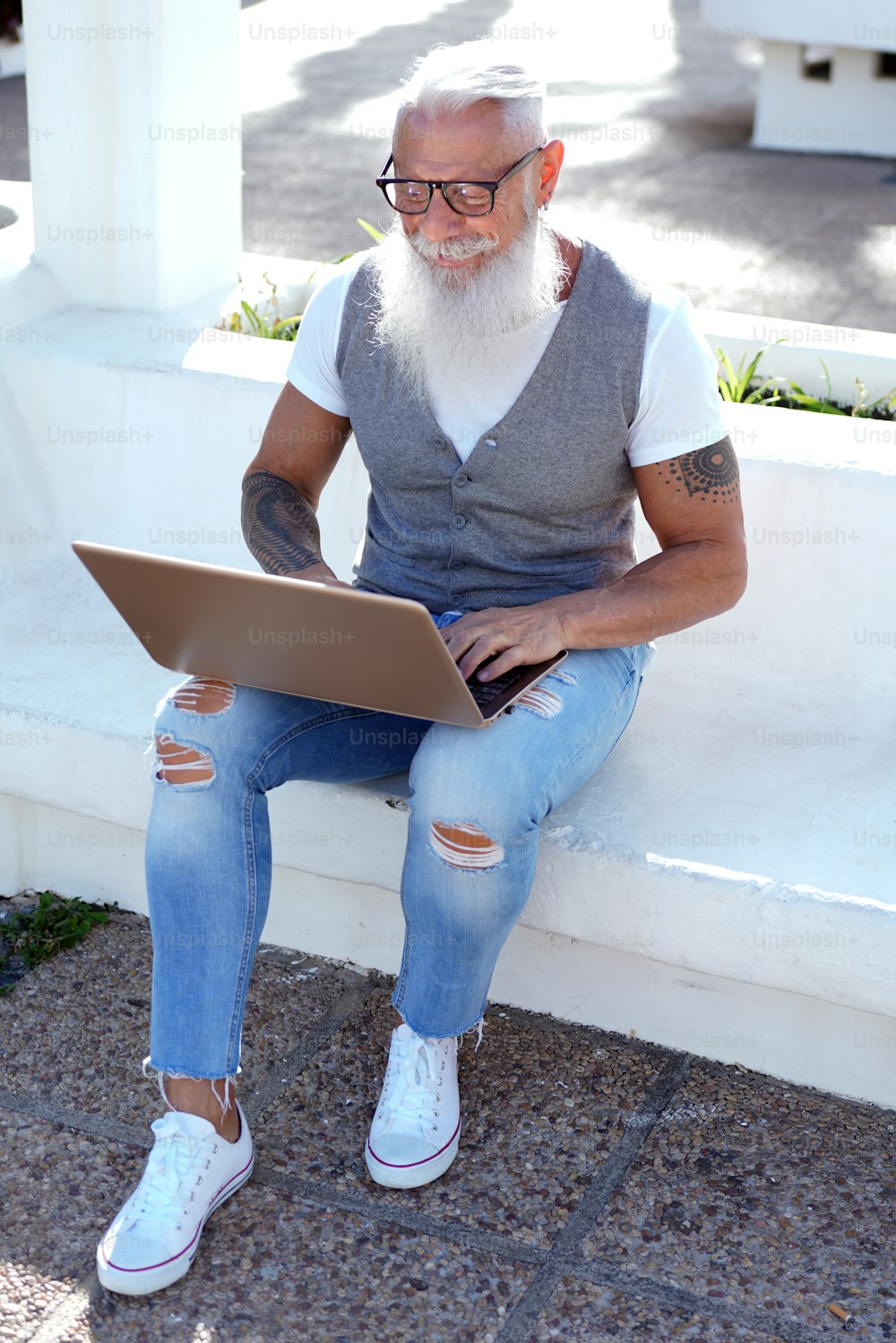 Senior fashionable man working on computer outdoor or talking with friends online. Sunny day. Handsome men with white beard and mustache.