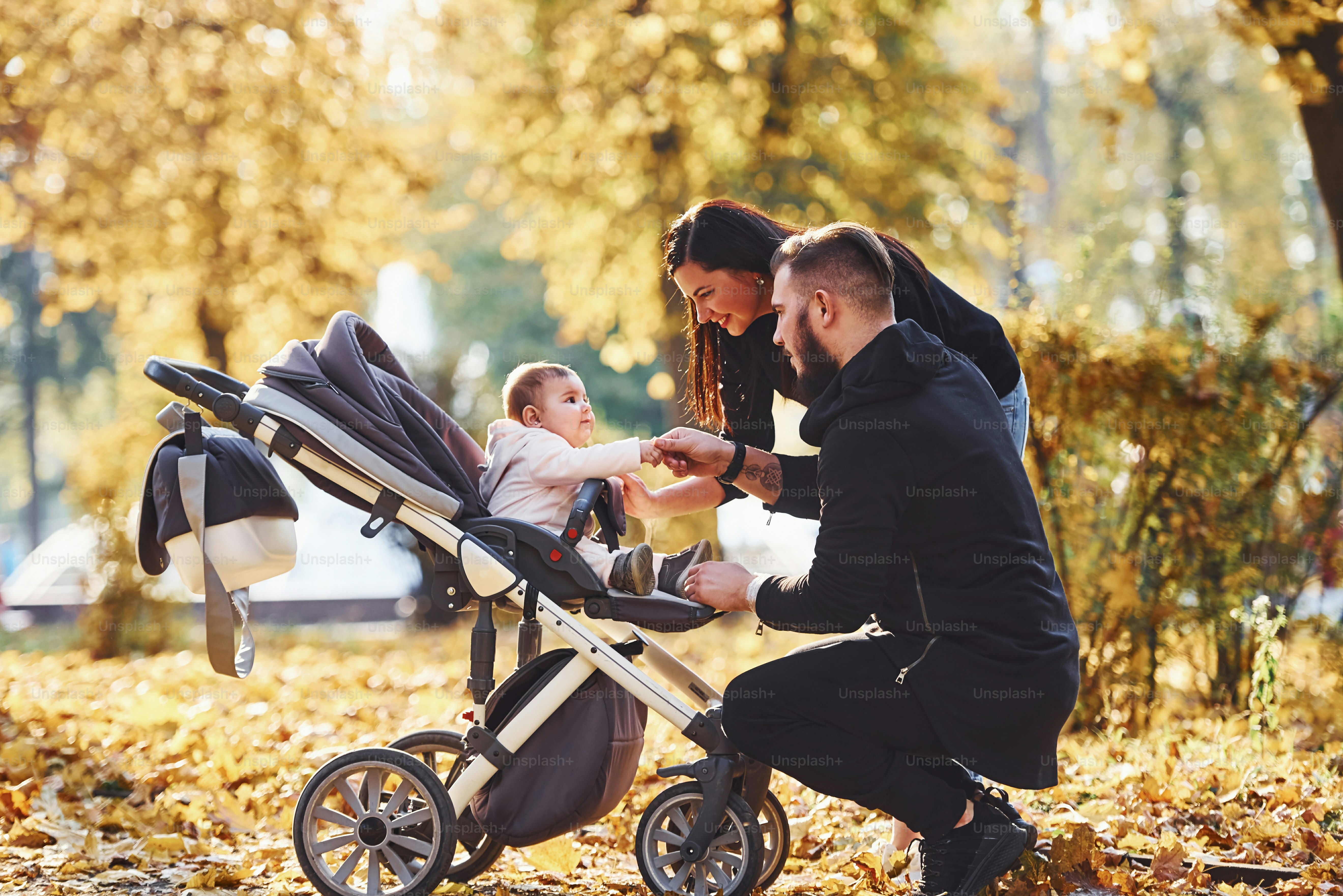 Cheerful family having fun together with their child in pram in beautiful autumn park.