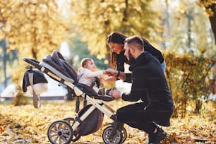 Cheerful family having fun together with their child in pram in beautiful autumn park.