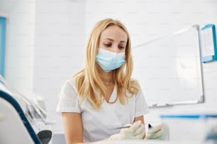 Female paying all her attention to the end of dental plugger entering bottle with resin composite