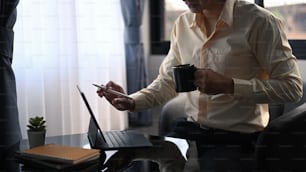 Foto cortada de um empresário feliz segurando uma xícara de café e usando o tablet do computador na sala do escritório.