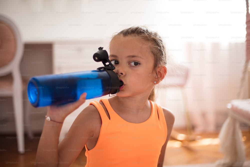 Little girl drinking water after exercise at home.