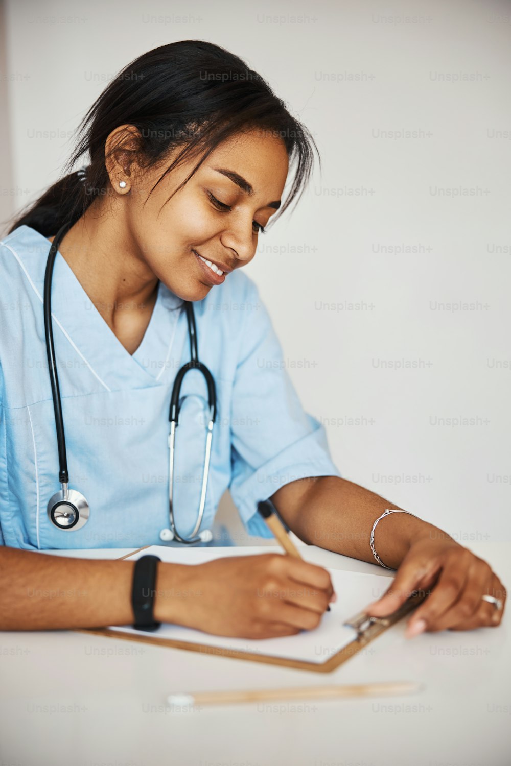 Schöne junge Ärztin, die das medizinische Formular des Patienten ausfüllt und lächelt, während sie am Tisch sitzt. Isoliert auf weißem Hintergrund
