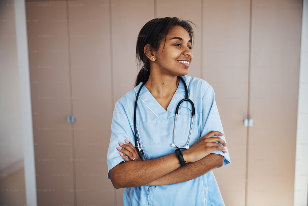 Charming Afro American young woman physician looking away and smiling while crossing arms over her chest